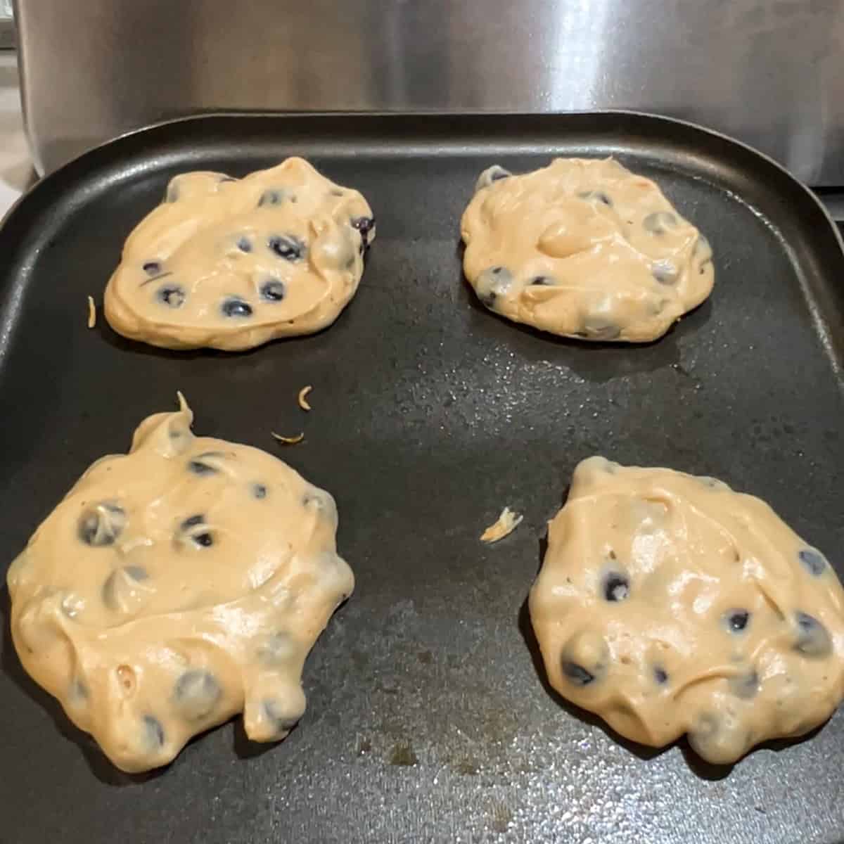 blueberry protein pancakes on a griddle just ready to be flipped.