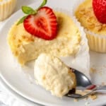 mini protein cheesecake topped with half a strawberry and a spoonful is being drawn from it.