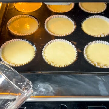 muffin tin with mini protein cheesecakes in oven on a baking sheet and water being poured in for the water bath.