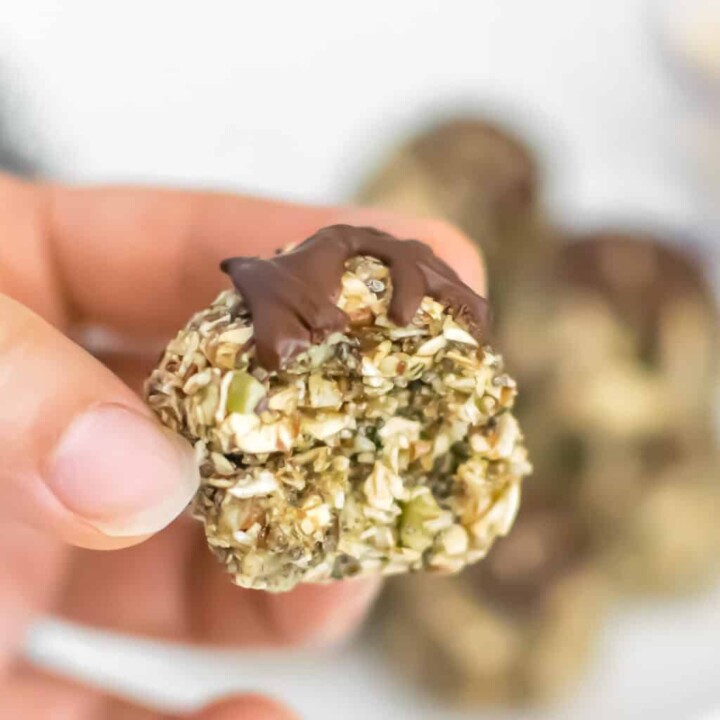 hand holding an oatmeal energy ball packed with seeds and topped with chocolate drizzle.