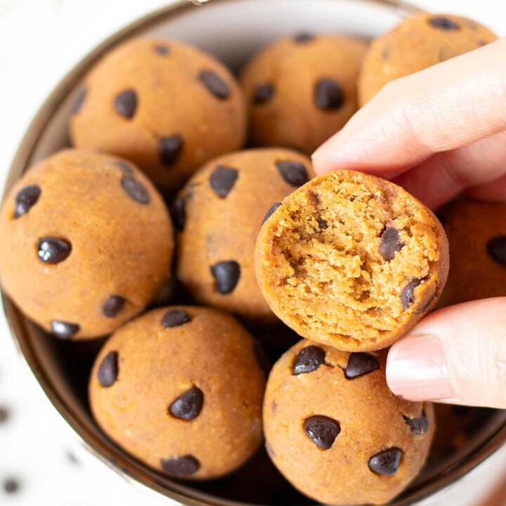 bowl of pumpkin protein balls with mini chocolate chips with one bitten ball being held in a hand.