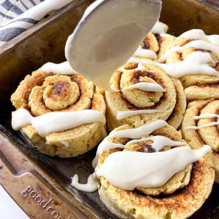 icing being spooned onto a pan of high protein cinnamon rolls.