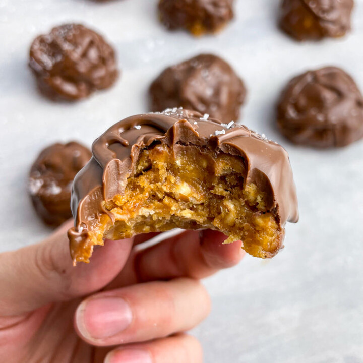 hand holding a bitten chocolate covered peanut butter granola bite.