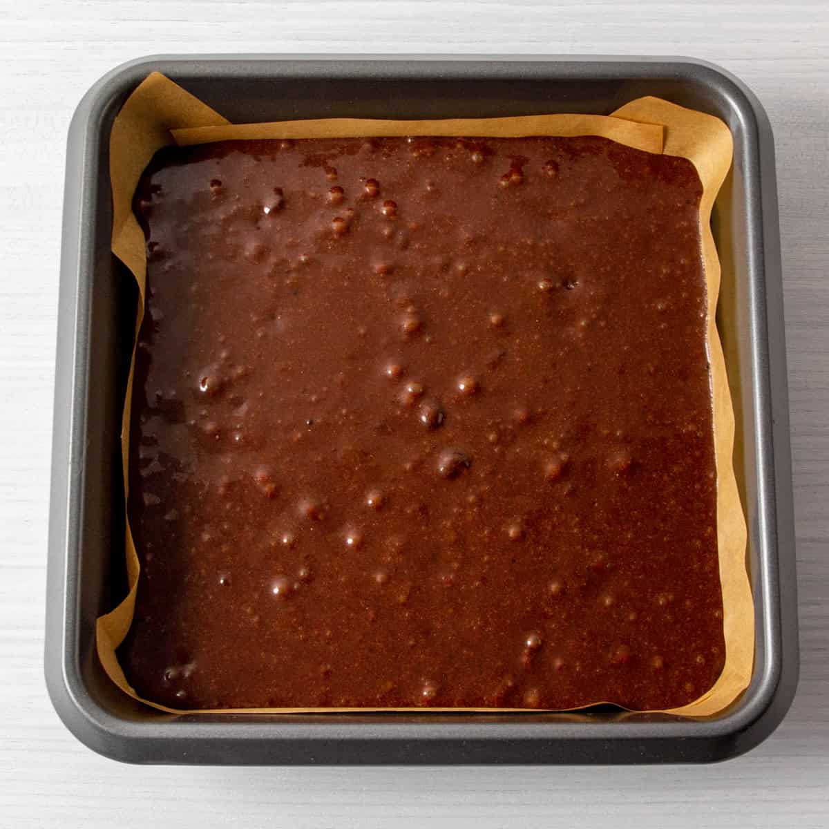 collagen protein brownie batter in a parchment lined pan, ready for baking.