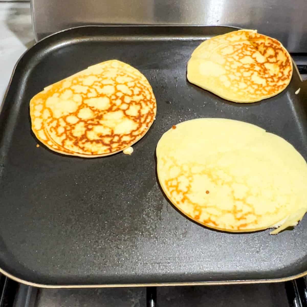 3 lemon ricotta protein pancakes on a griddle pan after being flipped.