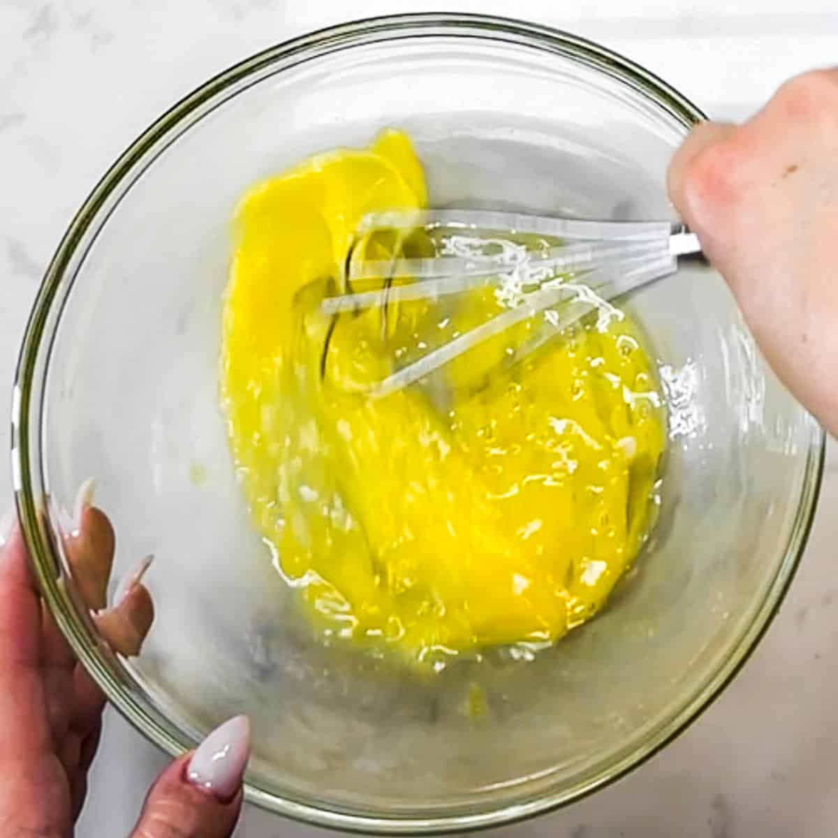 egg being beaten with a whisk in a glass bowl.