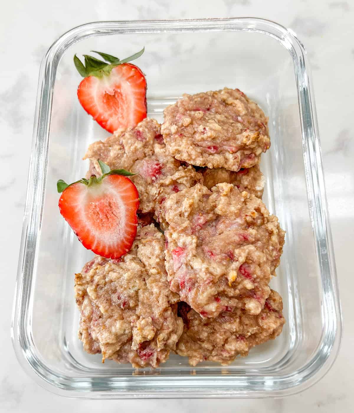 strawberry protein cookies in a glass meal pep container with two strawberry halves.