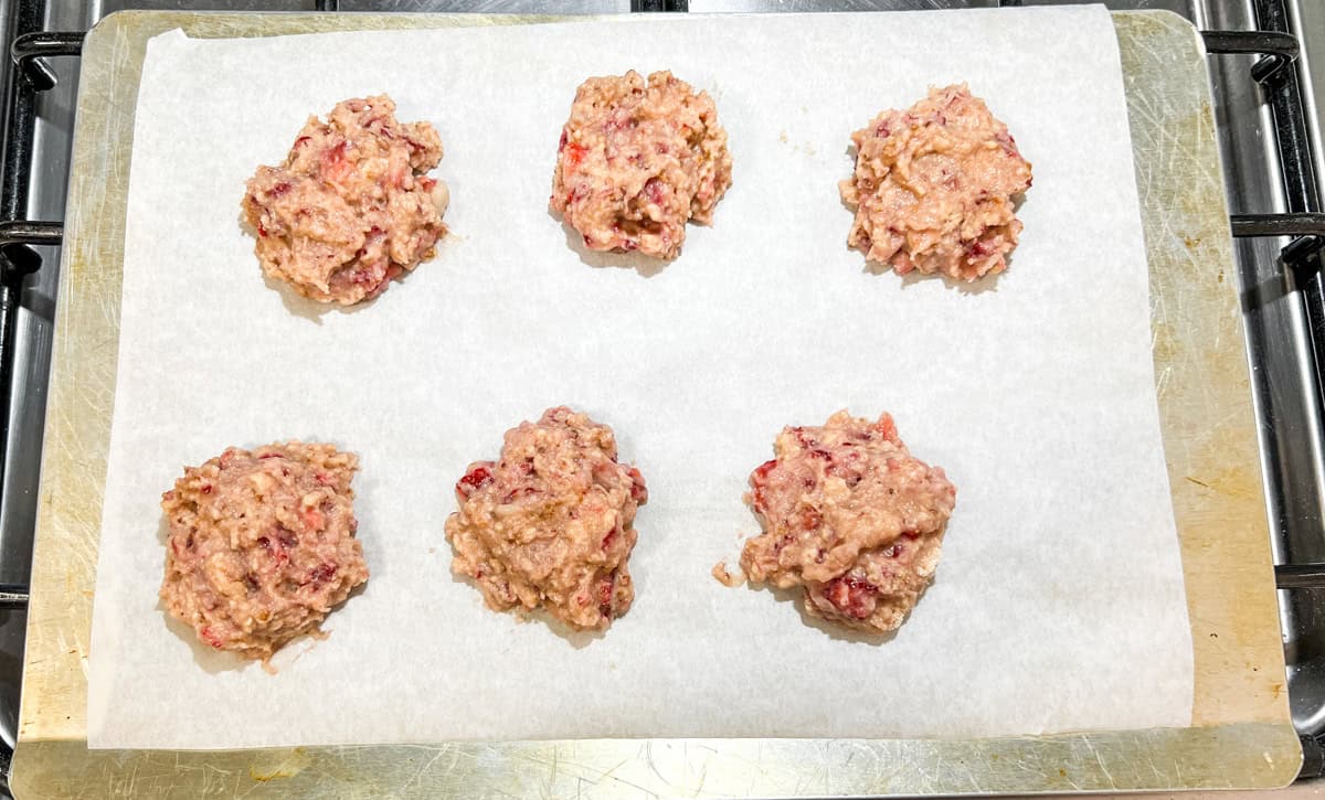 6 strawberry protein cookies, unbaked, on a parchment-lined cookie sheet.