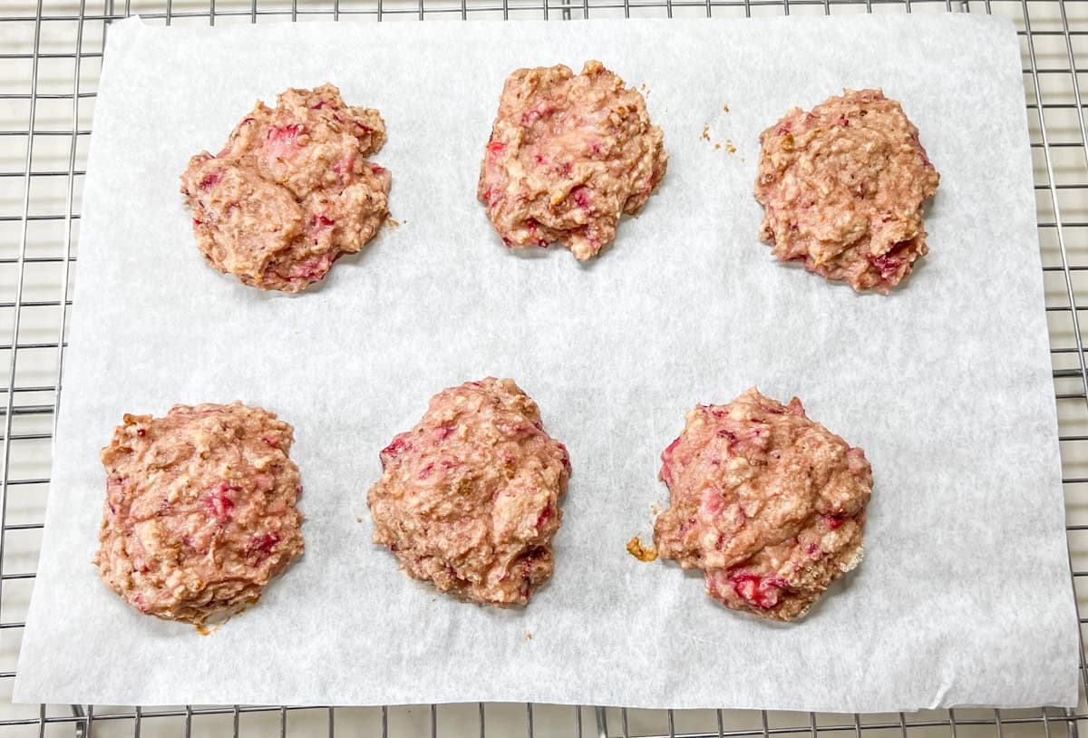 6 baked strawberry protein cookies on parchment on a wire cooling rack.