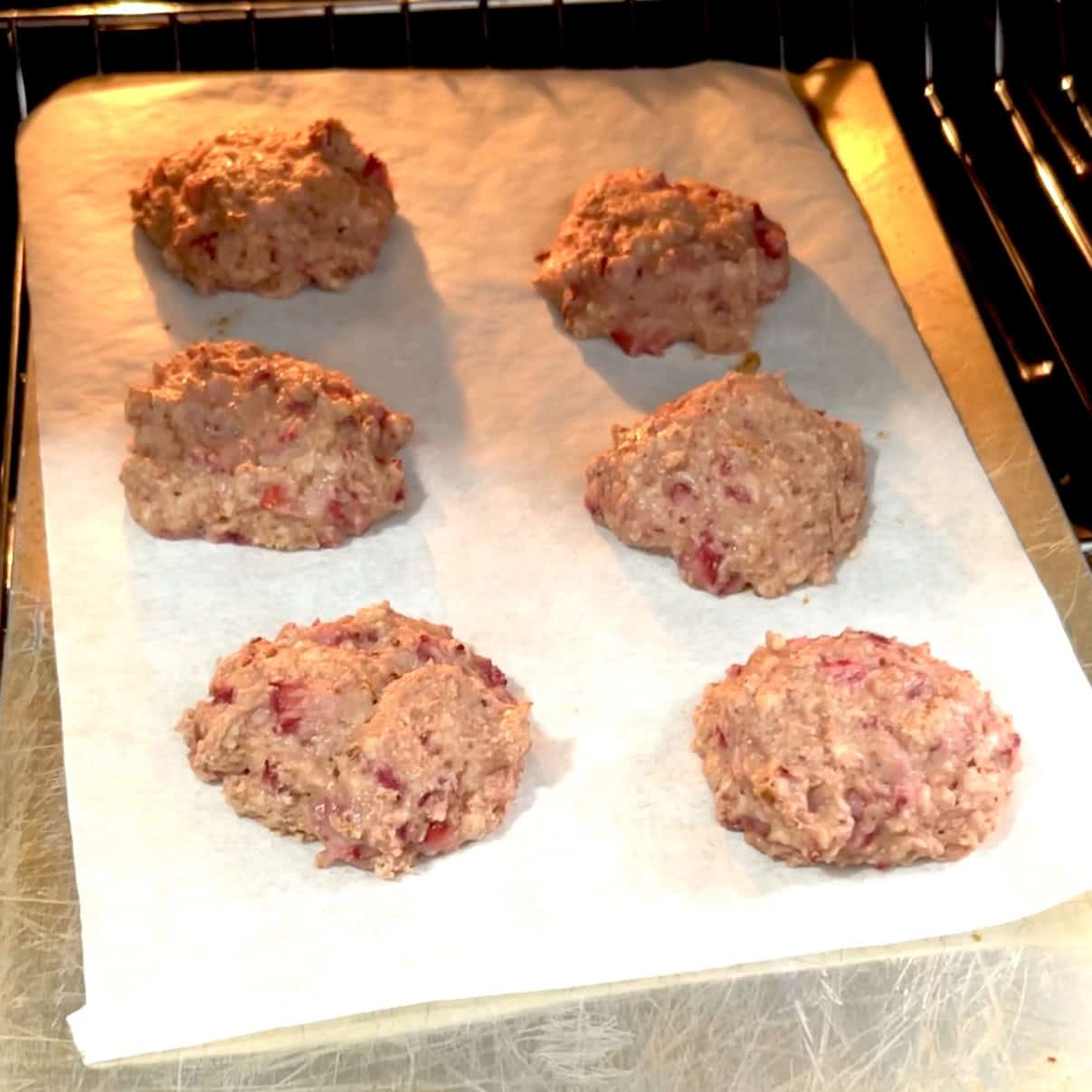 strawberry protein cookies on a parchment-lined cookie sheet in the oven.