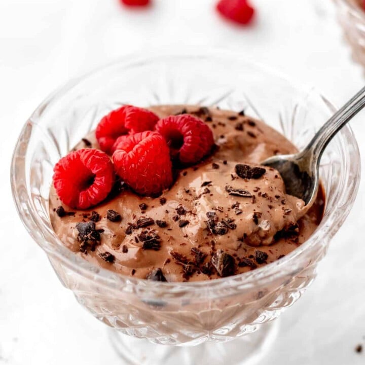 chocolate mousse with raspberries and shaved chocolate in a glass dessert dish.