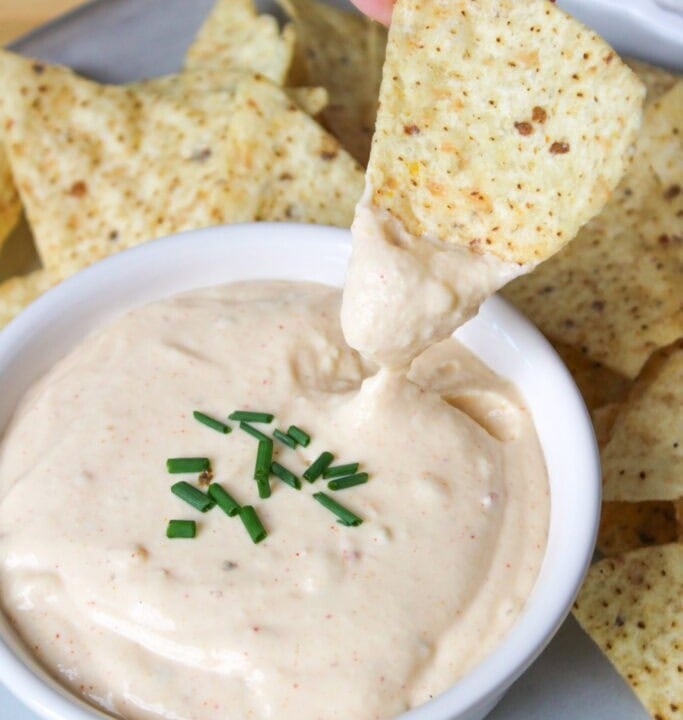 bowl of cottage cheese queso with a tortilla chip being dipped into it.