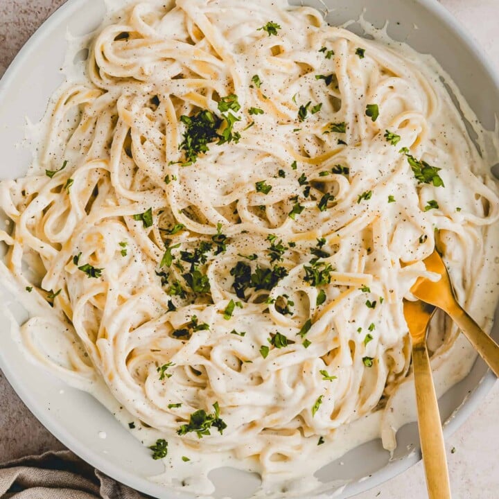bowl of fettuccini alfredo in a pan with serving utensils.