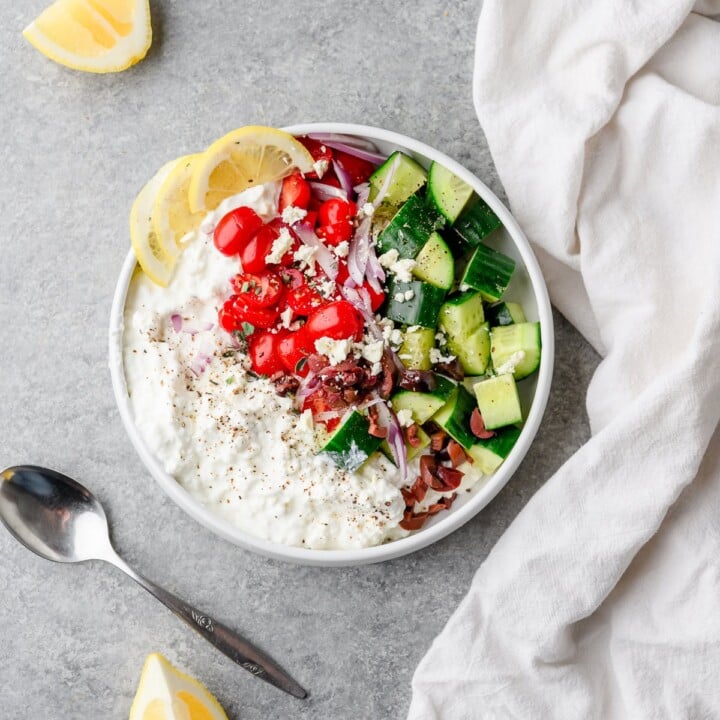 bowl of cottage cheese with tomato, cucumber, and lemon.
