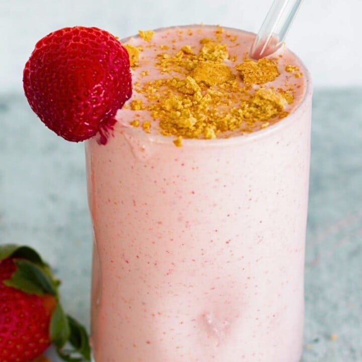 strawberry shake in a glass topped with a fresh strawberry and graham cracker crumbs.