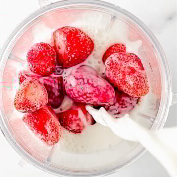 frozen strawberries in blender cup with almond milk pouring in.