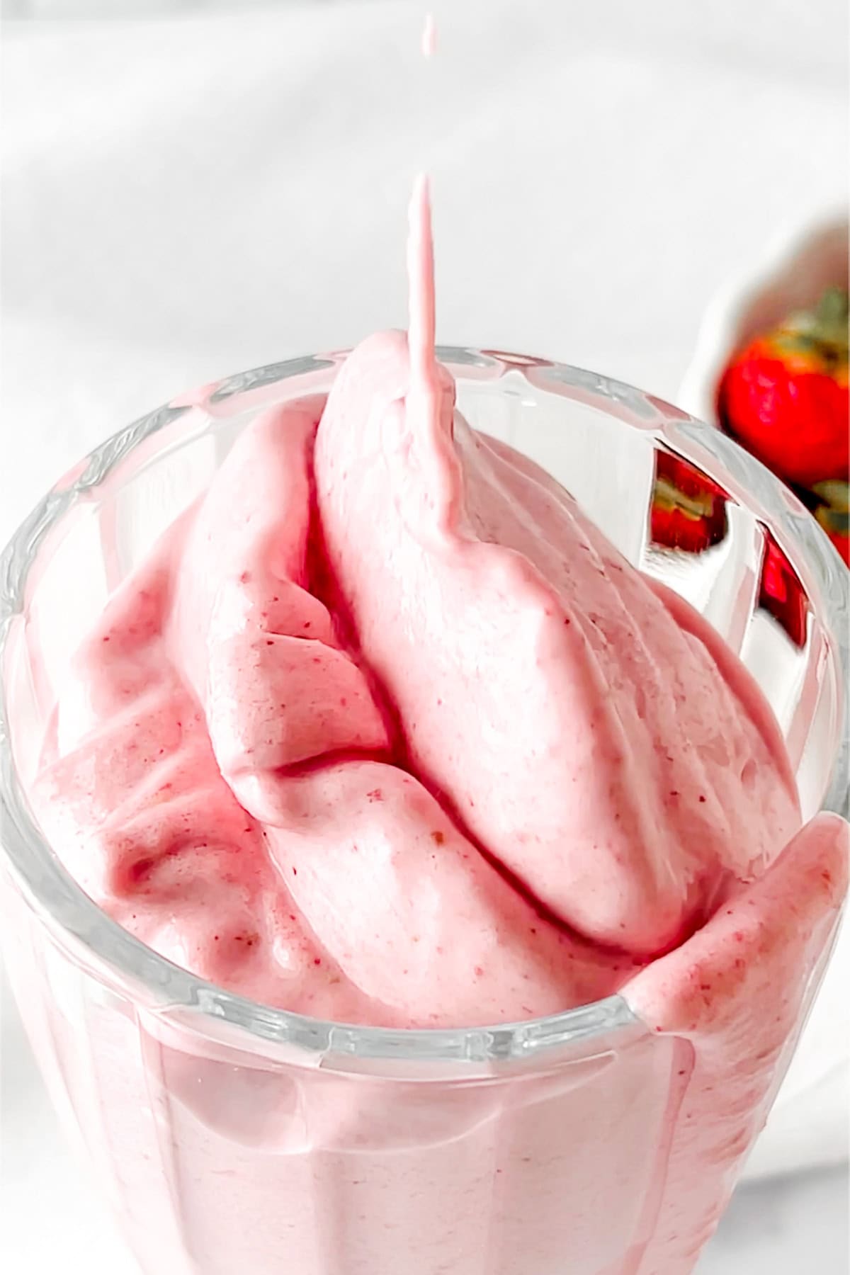 thick and creamy strawberry protein shake being poured into a milkshake glass.