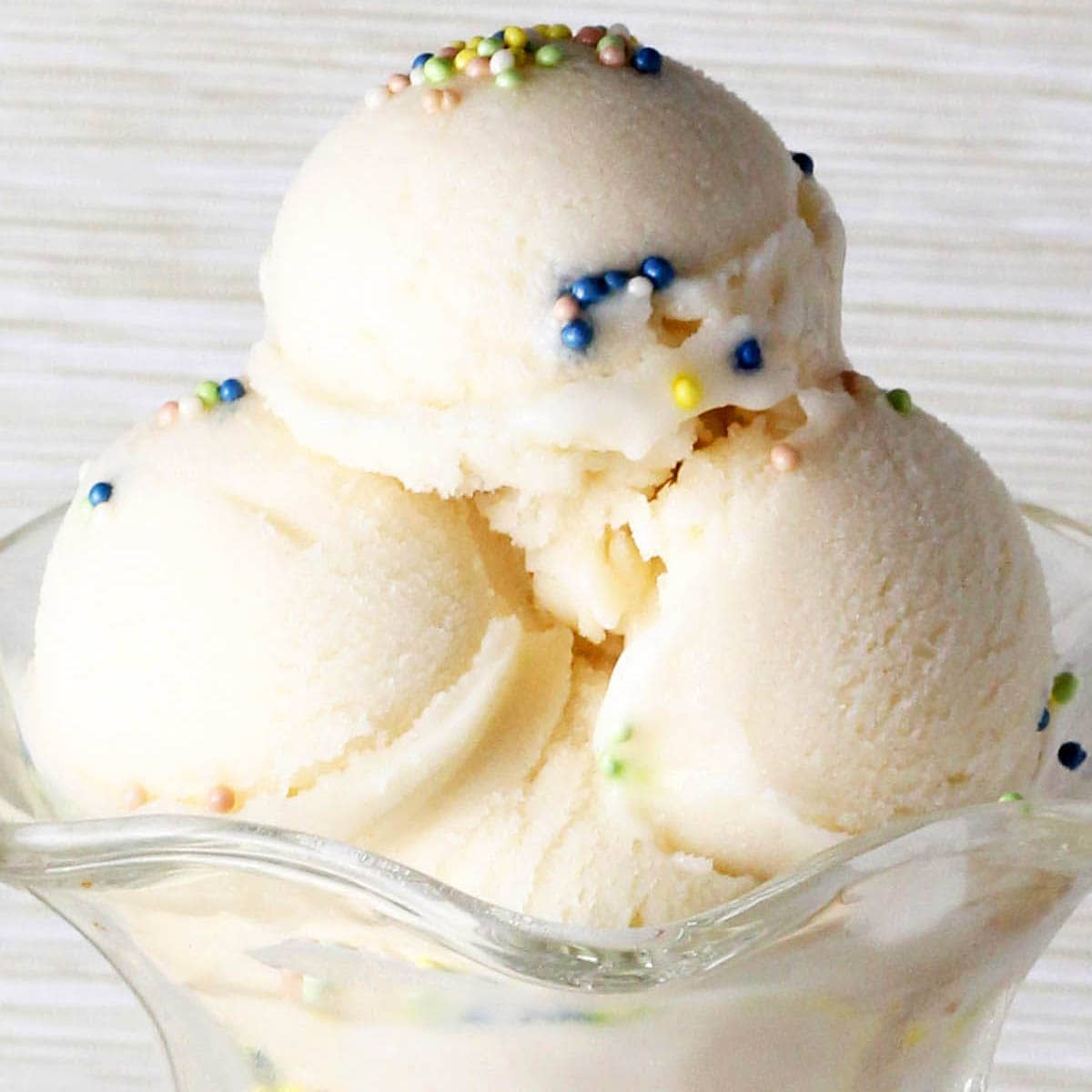 scoops of cake batter protein ice cream in a glass ice cream dish with sprinkles.