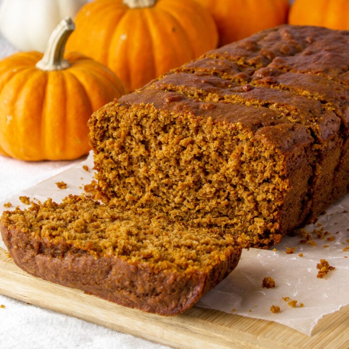 sliced loaf of high protein pumpkin bread on a cutting board surrounded by decorative mini pumpkins.