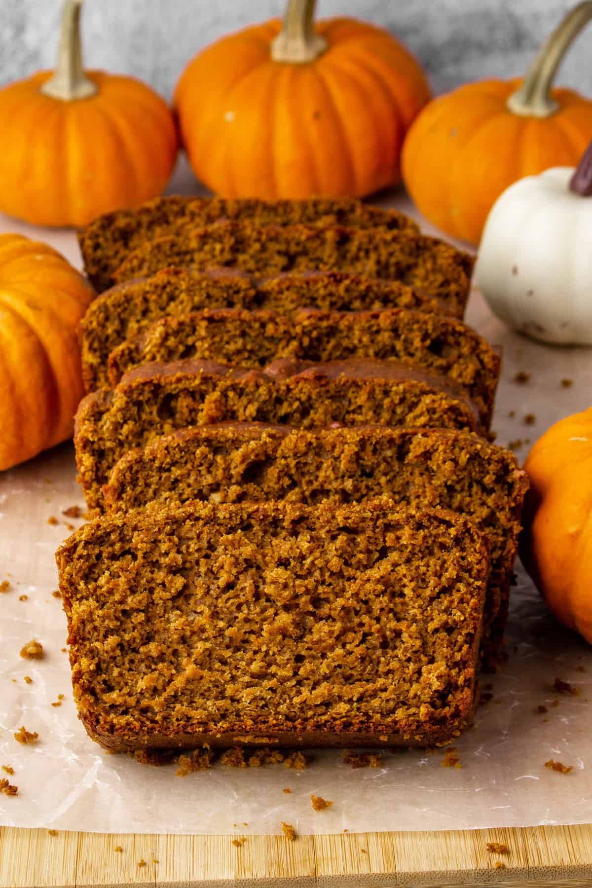 sliced loaf of high protein pumpkin bread on a cutting board surrounded by decorative mini pumpkins.