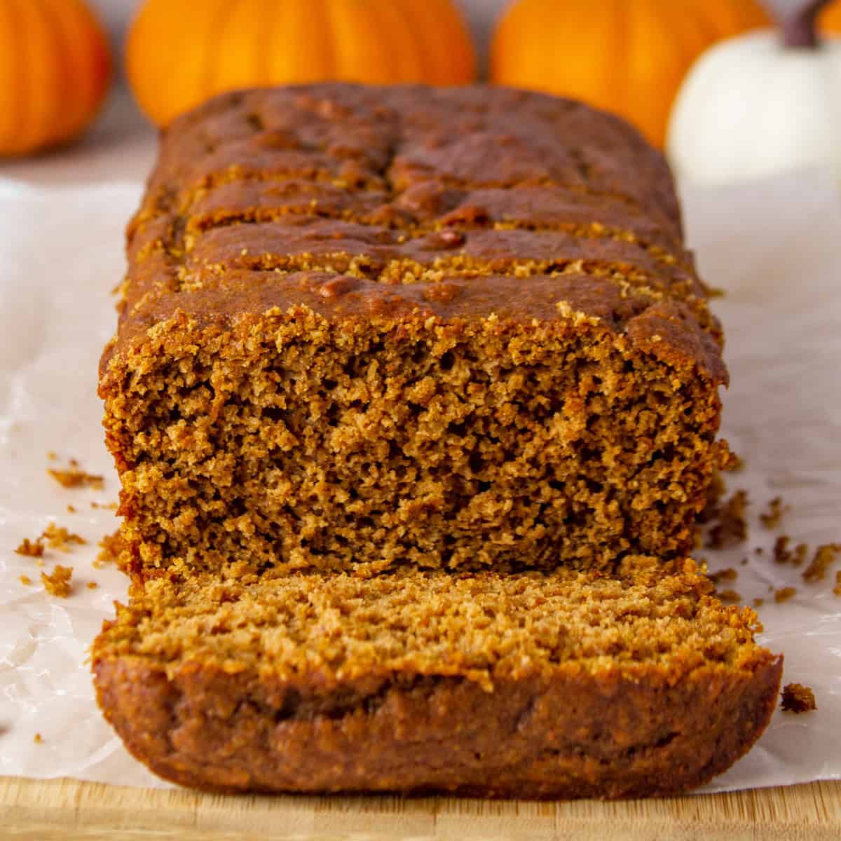 sliced loaf of high protein pumpkin bread on a cutting board surrounded by decorative mini pumpkins.