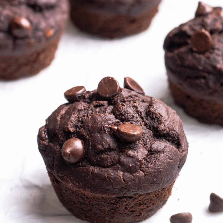 chocolate protein muffins with chocolate chips on a piece of parchment paper.