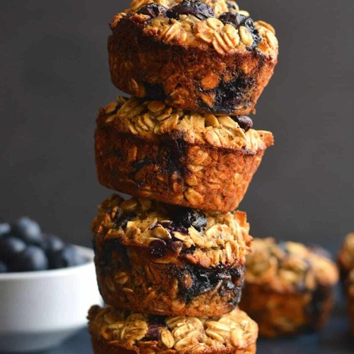 blueberry oat protein muffins stacked on a blue surface.