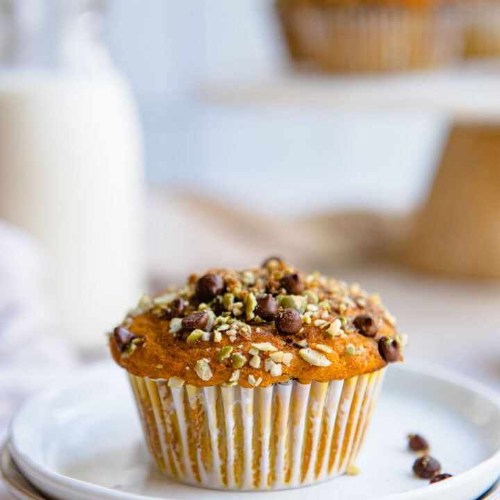 pumpkin protein muffin topped with pumpkin seeds and chocolate chips on a plate.