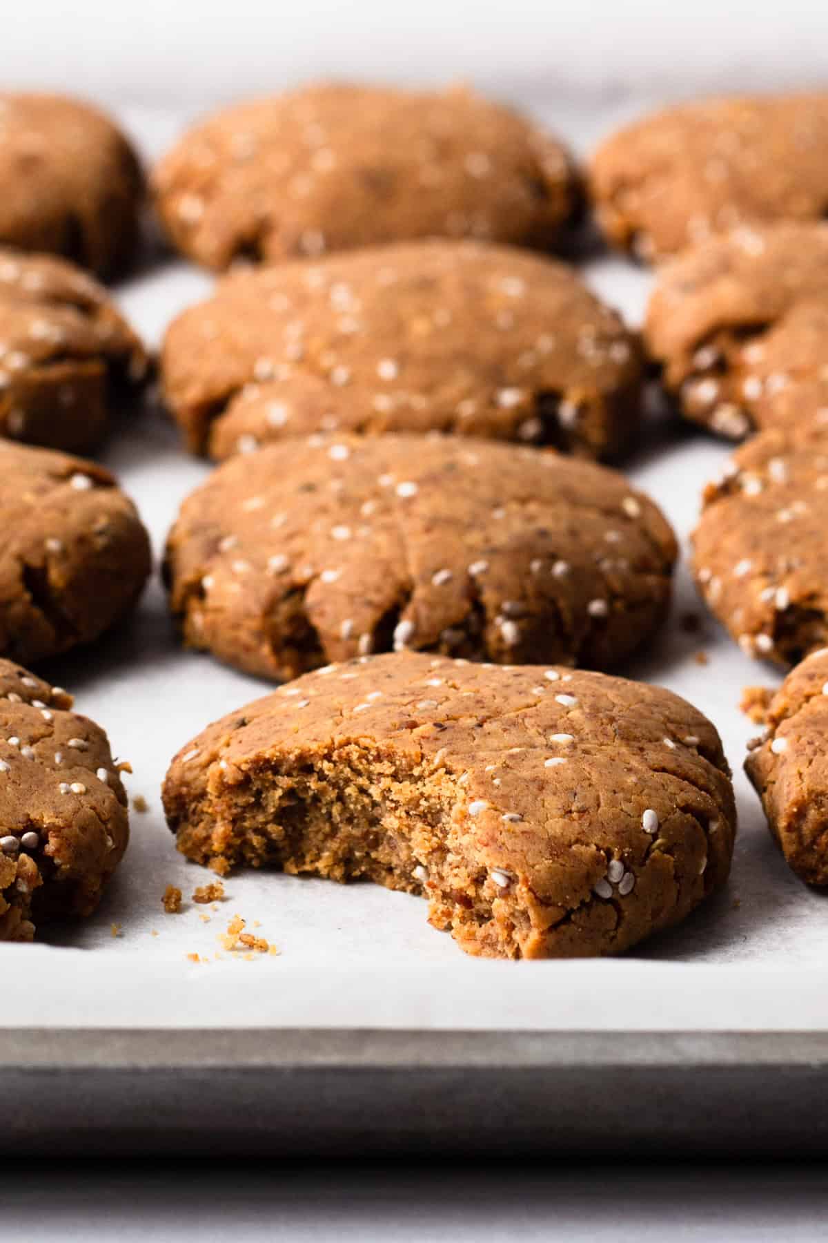 freshly baked chia almond protein cookies on a baking tray, one bitten.