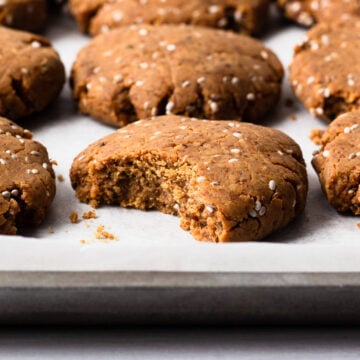 freshly baked chia almond protein cookies on a baking tray, one bitten.