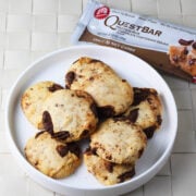 eight pieces of a chocolate chip cookie dough quest bar baked into cookies on a white plate and next to a packaged quest bar.