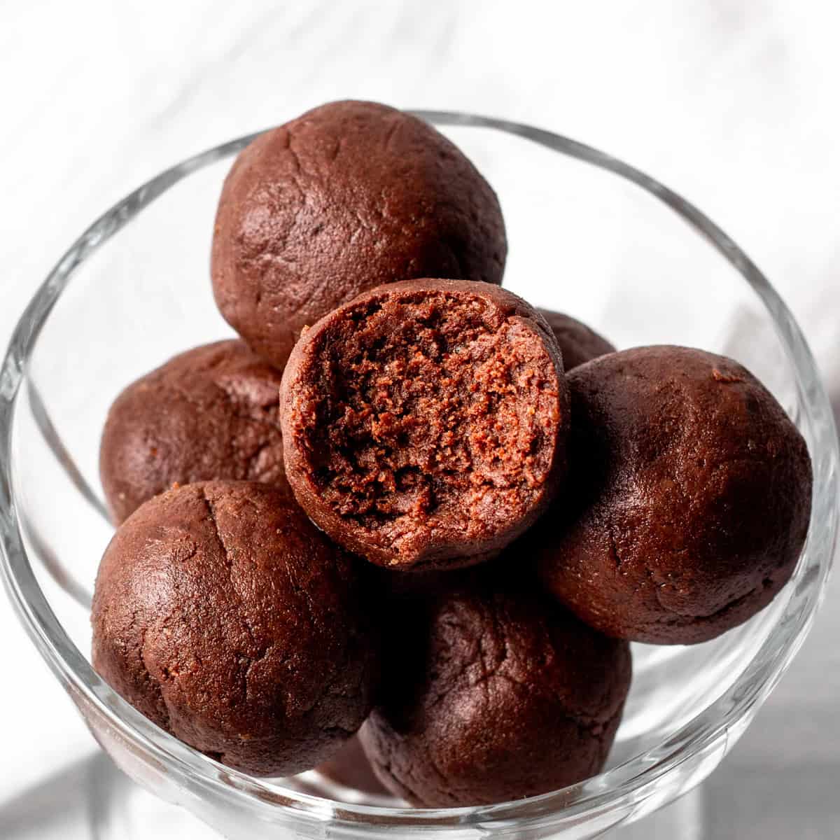 chocolate protein balls in a serving dish with one bitten.