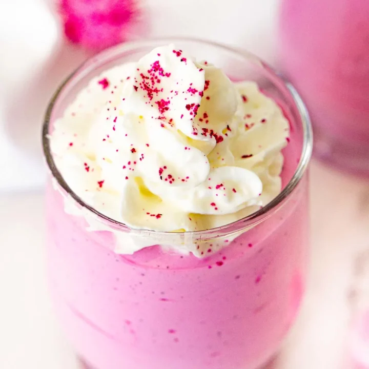 pink dragon fruit whipped dessert in a glass serving dish, topped with whipped cream.