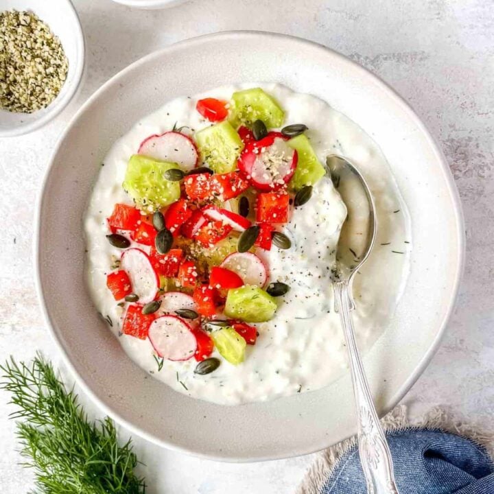 cottage cheese with cucumbers and red peppers in a bowl with a spoon.