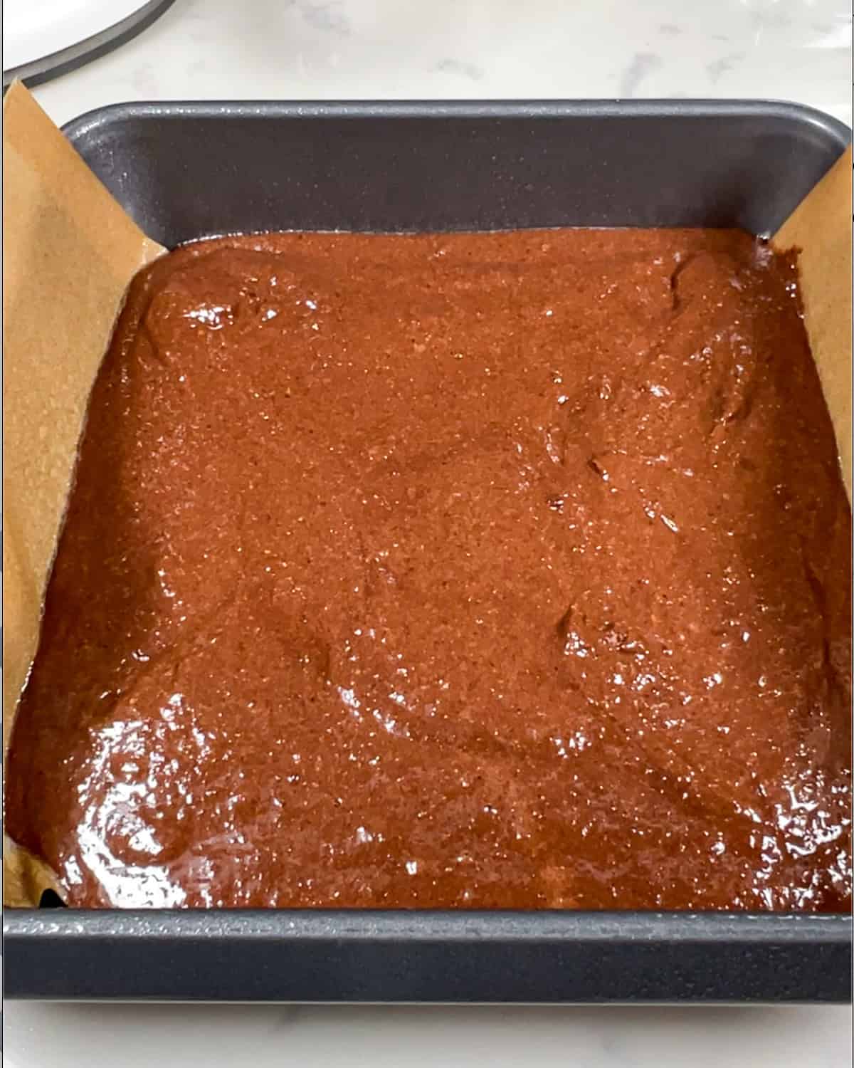 whey protein brownie batter in a pan, ready for the oven.
