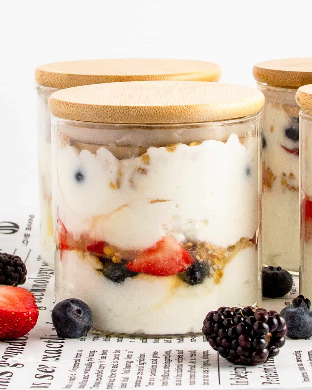 high protein breakfast parfait with yogurt, berries, and granola in a glass jar with bamboo lid.